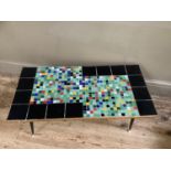 A mid century coffee table the top inset with black and mosaic tiles, edged in teak, on black