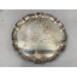 A George V silver waiter of circular scalloped outline with three scroll feet, contemporary