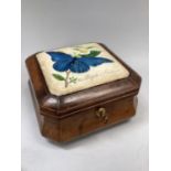 A tan leather covered casket of square outline, the cushioned lid inset with a square plaque painted