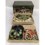 A dark green jewellery box containing a collection of necklaces, earclips and brooches with a velvet