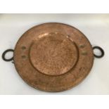 A large copper charger with dished centre and two iron ring handles, 51.5cm diameter