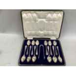 A box of twelve George V silver teaspoons with sugar tongs, ribbon thread pattern, hallmarked