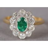 AN EMERALD AND DIAMOND CLUSTER RING, the oval faceted emerald millegrain set within a surround of