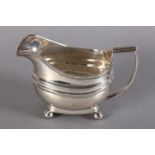 A GEORGE III SILVER CREAM JUG of oblong form with gadroon rim and reeded handle and on four bun