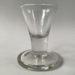 A MID 18TH CENTURY FIRING GLASS, the bucket bowl drawn into a short solid stem on a thick conical