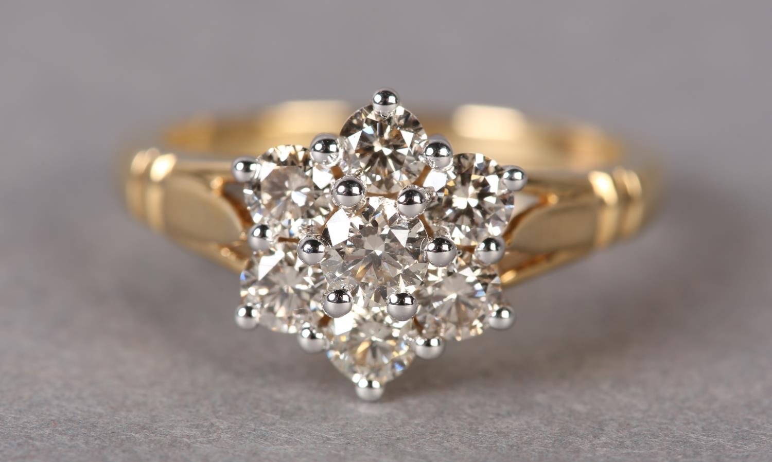 A DIAMOND CLUSTER RING the brilliant cut stones claw set within a circular outline flanked by