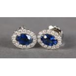 A PAIR OF SAPPHIRE AND DIAMOND CLUSTER EARRINGS in 18ct white gold, each claw set to the centre with