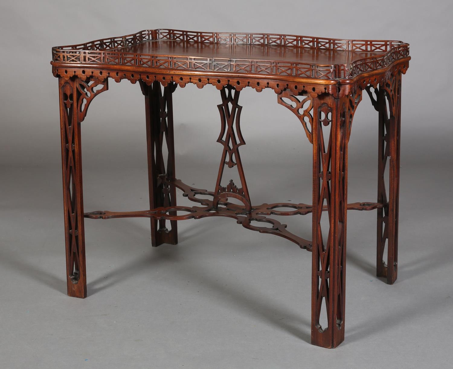 A GEORGE III MAHOGANY TEA TABLE of rectangular serpentine outline with fretwork gallery apron, angle