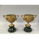 A PAIR OF 19TH CENTURY ORMOLU TWIN HANDLED PEDESTAL URNS, cast in high relief with opposing