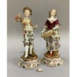 A pair of Continental porcelain figures in 18th century dress on plinth bases, the woman carrying