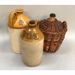 Two stoneware flagons and wine bottle in wicker basket, the flagons brown glaze dipped, one stamped,