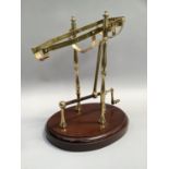 A brass wine decanting cradle with rotating mechanism on mahogany base, 35cm high