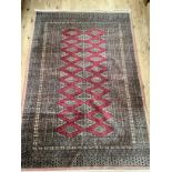 A Middle Eastern Bokhara rug having a crimson ground filled with lozenge medallions within a