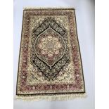 A Middle Eastern silk rug in ivory, camel, black and maroon, the black field filled with a flower