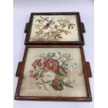Two trays each inset with a needlework panel, in oak frames, one depicting two birds in foliage