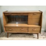 A mid century teak sideboard with glass folding doors revealing internal glass shelves flanked by