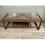 A mid century teak coffee table, the top inset with brown tiles, glass top and railed undertier,