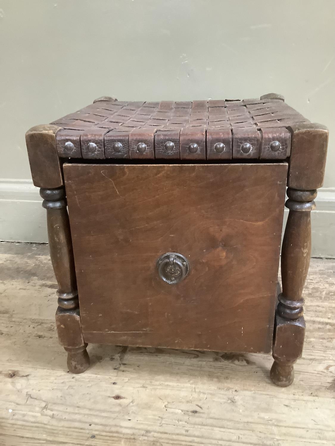 An oak slipper box stool with ring pull handle and top of interwoven leather studded to the side