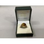 A signet ring in 9ct gold, collet set with an oval tiger eye stone, flanked by textured shoulders,