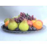 A glass platter and quantity of fake fruit to include grapes, pears, oranges, apples and cherries,