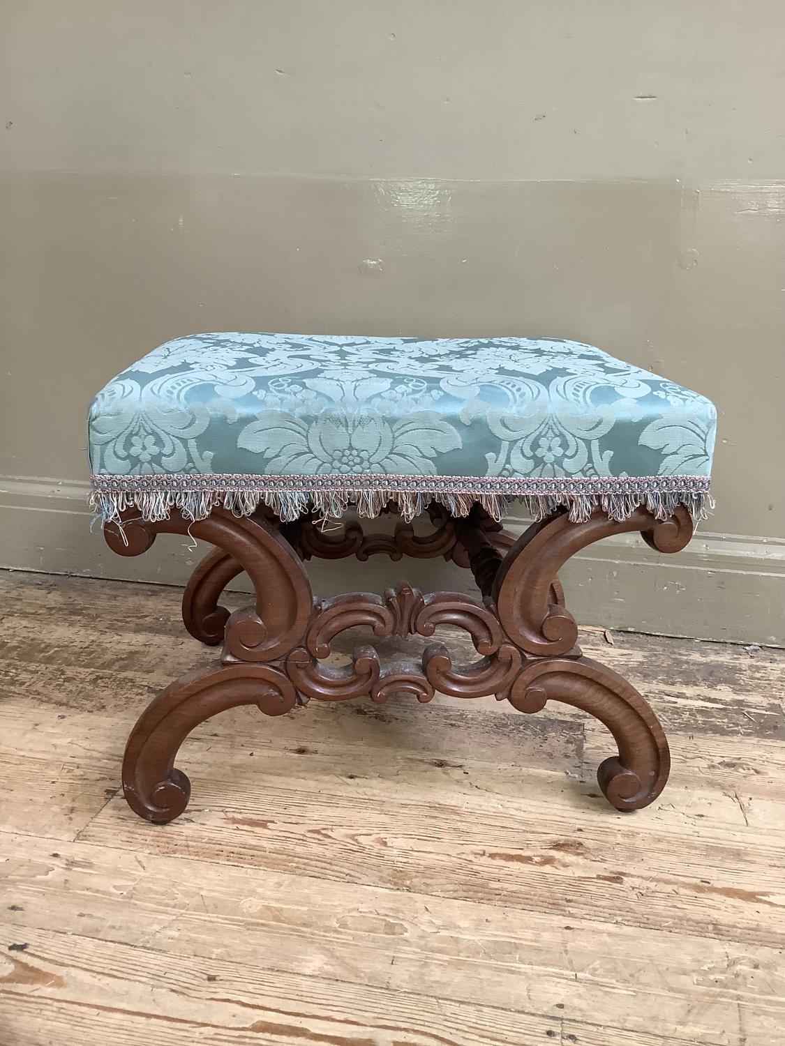 A Victorian mahogany heavily carved stool with c-scroll legs joined by turned supports,