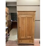 A stripped pine single wardrobe with a hanging cupboard on one draw. On bun feet with brass