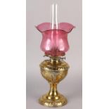 A VICTORIAN BRASS OIL LAMP, with rocaille and scroll reservoir, on conforming base, cranberry