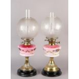 A NEAR PAIR OF VICTORIAN BRASS OIL LAMPS, the pink tinted reservoirs painted with mauve flower heads