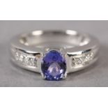 A TANZANITE AND DIAMOND RING in 18ct white gold by Iliana, claw set to the centre with an oval