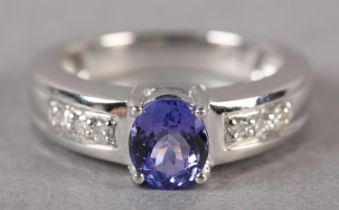 A TANZANITE AND DIAMOND RING in 18ct white gold by Iliana, claw set to the centre with an oval