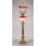 A VICTORIAN BRASS CORINTHIAN COLUMN OIL LAMP, pink tinted and gilt floral reservoir, on stepped