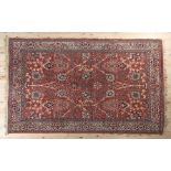 A MIDDLE EASTERN RUG, the deep coral field filled with opposing design of vases of flowers and