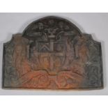 A CAST IRON ARCHED HERALDIC FIREBACK moulded in relief with central shield flanked by trailing