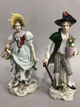 A pair of Sitzendorf porcelain figures depicting a man holding a plant pot and spade with flowers at