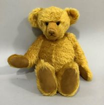 A golden plush bear with hump back and centre seam, boot button eyes, stitched snout, jointed body