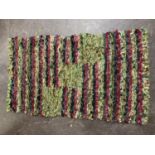 A rag rug, 78cm by 130cm approximately, in several colours, predominately shades of green, raspberry