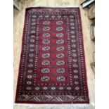 A wool Middle Eastern rug, having cream rosettes on a burgundy field with geometric border 153cm x