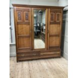 An Edwardian walnut triple wardrobe having central mirrored panel with fitted interior of two slides
