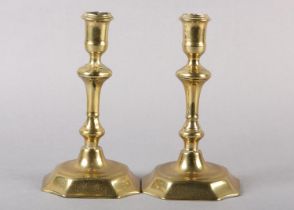 A pair of early 18th century brass candlesticks, having a cylindrical sconce, inverted baluster stem