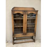 An early 20th century oak glazed bookcase on barley twist supports with stretcher and carved back