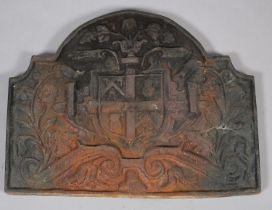 A cast iron arched heraldic fireback moulded in relief with central shield flanked by trailing