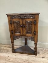 A reproduction oak free standing corner cupboard with carved front, two doors above pot base on