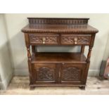 An oak two tier sidebord having two carved drawers above open recess above two doors with turned