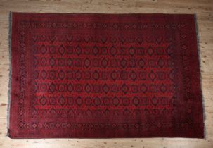 AN AFGHAN CARPET, modern, in shades of red and touches of blue, the red ground having seven rows