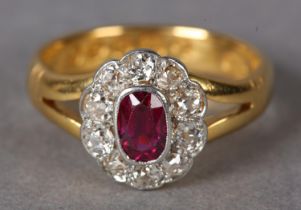 A RUBY AND DIAMOND CLUSTER RING, c1930, collet set to the centre with an oval faceted ruby within