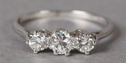 A THREE STONE DIAMOND RING c1955, the graduated brilliant cut stones claw set in line flanked by