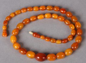 AN EARLY 20TH CENTURY AMBER NECKLACE in graduated oval beads with turned screw thread fastener (at