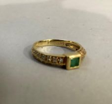 An emerald and diamond ring, the square facetted emerald at fault, flanked by brilliant cut