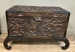 An early 20th century camphor wood chest on stand, heavily carved in relief with dragons chasing the