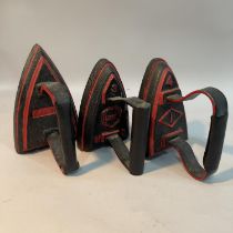 Three flat irons painted in black and red, one by Carron No.5, a Lyn WC3 and another numbered 4